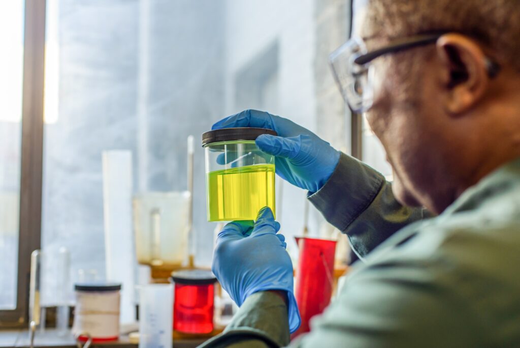 Lab technician inspecting beaker of yellow biofuel in biofuel plant laboratory